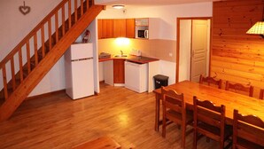Una cucina compatta con mobili in legno, un frigorifero bianco, un forno a microonde e un lavello. Un tavolo da pranzo in legno con sedie è posizionato di fronte alla cucina.