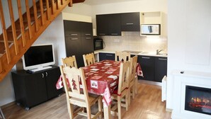 A compact kitchen with dark cabinets, a microwave, a small TV, and a dining area with a red tablecloth.