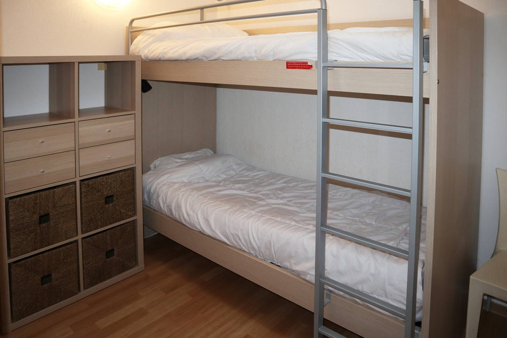 A bunk bed with a wooden ladder, a small desk, and storage drawers.