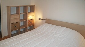 A neatly made bed with a wooden headboard and a bedside table with drawers and baskets.