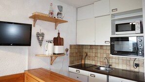 A compact kitchen with white cabinets, a wooden countertop, a built-in microwave, a toaster, and a TV mounted on the wall. - Studio 4 Personnes en Cœur de Station (LES ORRES 1650)