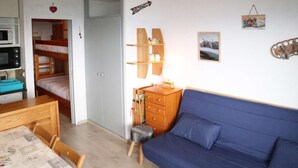 A compact room with a bunk bed, a sofa, a wooden cabinet, a small stool, and a table with chairs. - Studio 4 Personnes en Cœur de Station (LES ORRES 1650)