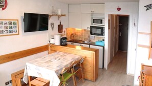 A compact kitchen with a microwave, stove, and sink. There is a dining table with benches and a TV mounted on the wall. - Studio 4 Personnes en Cœur de Station (LES ORRES 1650)