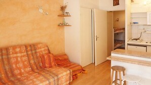 Een gezellige kamer met een bank, een kitchenette en een deur naar een andere kamer.
