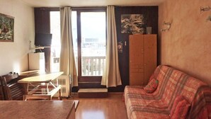 Een kamer met een houten tafel, een bank, een radiator, een televisie en uitzicht door een raam met gordijnen.