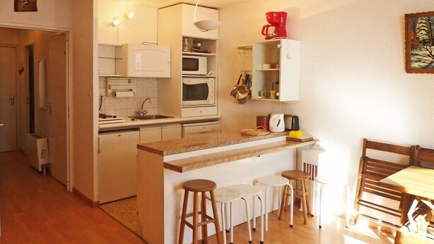 Een kleine keuken met witte kasten, een houten aanrechtblad en een eethoek met een houten tafel en stoelen.