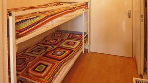 Een stapelbed met kleurrijke dekens, een witte deur en een houten vloer.