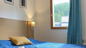 A bedroom with a single bed, a headboard, a nightstand, a lamp, two framed pictures on the wall, and a window with curtains.