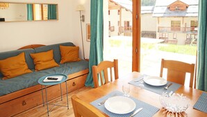 A cozy room with a sofa, a dining table set for two, and a view of a building with balconies.