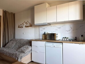 A compact kitchen with white cabinets, a microwave, a dishwasher, and a small countertop with a knife block and plants.