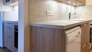 A modern kitchen with wooden cabinets, a built-in oven, a stainless steel sink, and a dishwasher.