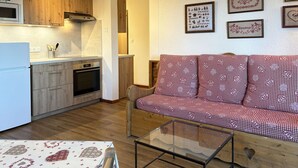 A compact living space with a kitchenette, a sofa, and a glass coffee table.