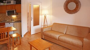 Un espace de vie compact comprenant un canapé en bois, une petite table en bois, un coin cuisine avec un four à micro-ondes et un grille-pain, ainsi qu’un miroir fixé au mur.