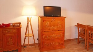 Une commode en bois ornée de motifs floraux, un téléviseur posé dessus, une lampe et une chaise.