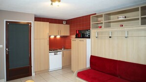 A compact kitchen with a dishwasher, a red sofa, and wooden cabinets. - Studio N° 211 LES Flocons (LES ORRES 1650)
