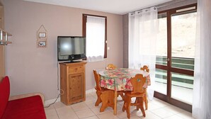 A dining area with a table set for four, a television on a wooden cabinet, and a sliding glass door to the outside. - Studio N° 211 LES Flocons (LES ORRES 1650)
