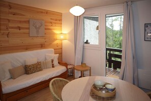 A cozy room with a wooden wall, a white sofa, a round table with bowls, and a window with curtains.