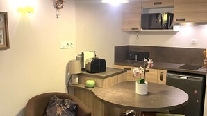 Een kleine keuken met een magnetron, broodrooster en koffiezetapparaat op het aanrecht. Er staat een eettafel met twee stoelen en een bijzettafeltje.