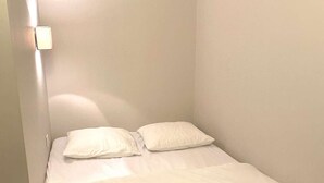 Een klein, net bed met witte lakens in een hoek slaapkamer met witte wanden en een houten vloer.