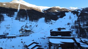 Een besneeuwde ski-resort met een skilift, gebouwen en bergen op de achtergrond.
