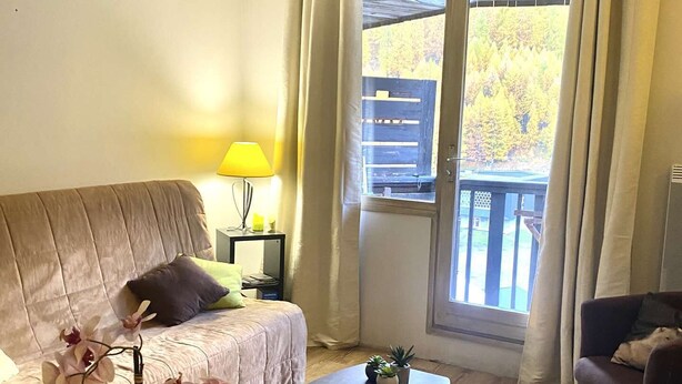 Een woonkamer met een bank, een salontafel, een lamp en uitzicht op een balkon.