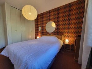 A bedroom with a large bed, a wardrobe, a round mirror, and a wall with a pixelated pattern.