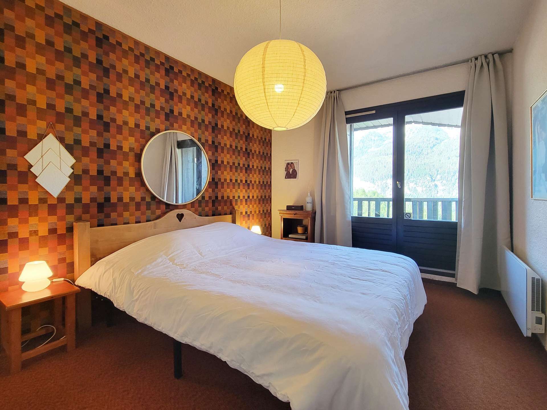 Habitación de hotel con una cama grande, un espejo redondo, un cuadro colgado en la pared y una ventana con cortinas.