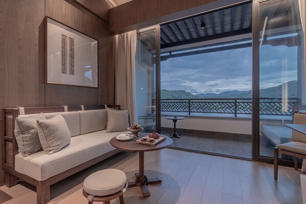 A modern living room with a sofa, a small round table with a tray of snacks, and a view of a balcony with a railing and a body of water in the background. - Grand Dongshan (Shaoxing)