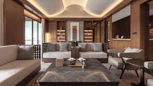 A modern living room with a sofa, armchairs, and a coffee table. There is a bookshelf with decorative items and a large mirror. - Grand Dongshan (Shaoxing)