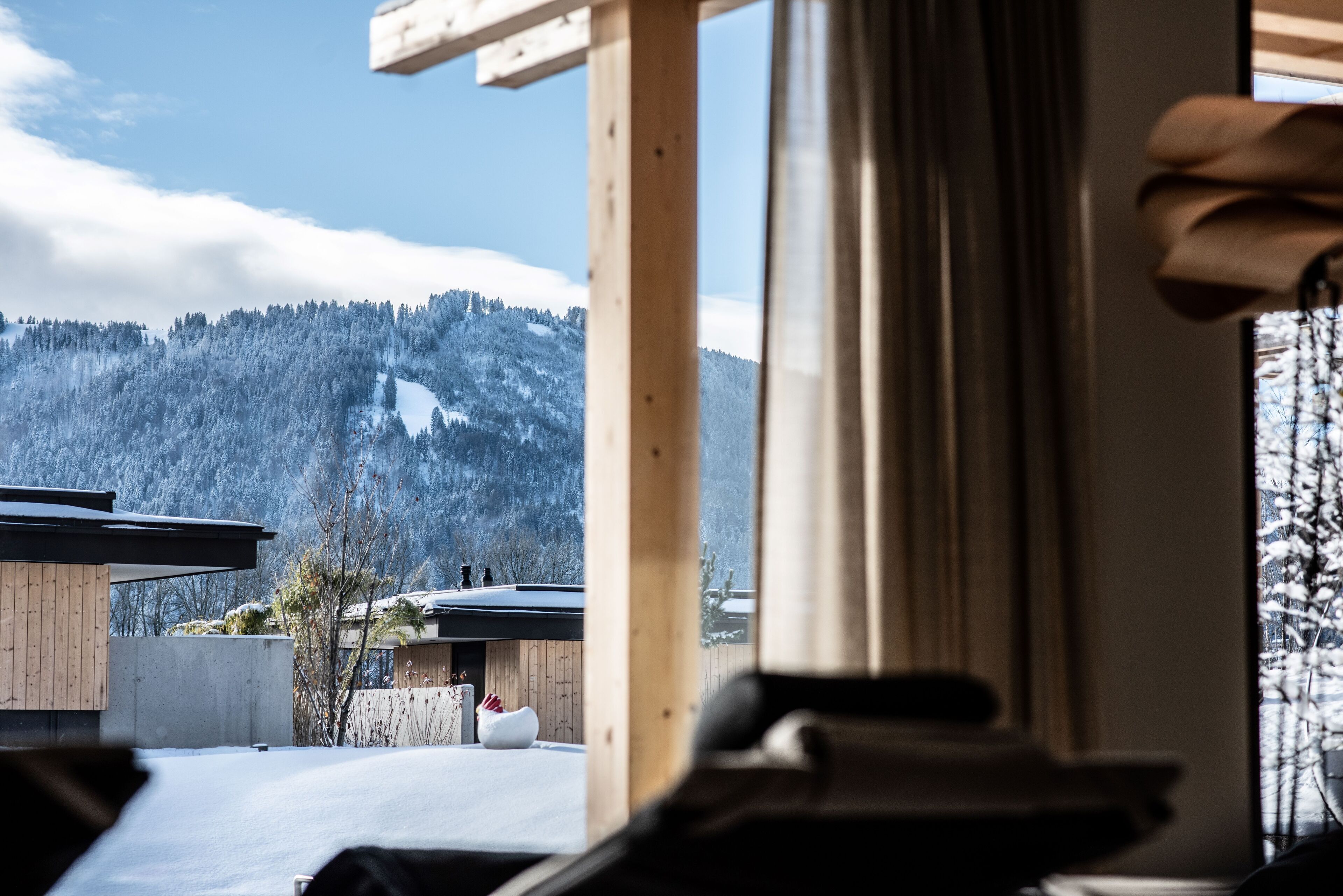 A view of a snowy mountain landscape through a window, with a wooden structure in the foreground.