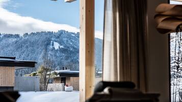 A view of a snowy mountain landscape through a window, with a wooden structure in the foreground.