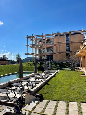 A pool area with lounge chairs and umbrellas, surrounded by a well-maintained lawn and a building under construction. - Hotel BERGEBLICK  (Bad Toelz)