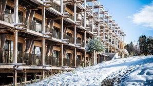 A multi-story wooden building with balconies, a ski slope in the foreground, and a clear blue sky. - Hotel BERGEBLICK  (Bad Toelz)
