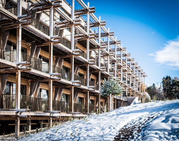 A multi-story wooden building with balconies, a ski slope in the foreground, and a clear blue sky. - Hotel BERGEBLICK  (Bad Toelz)