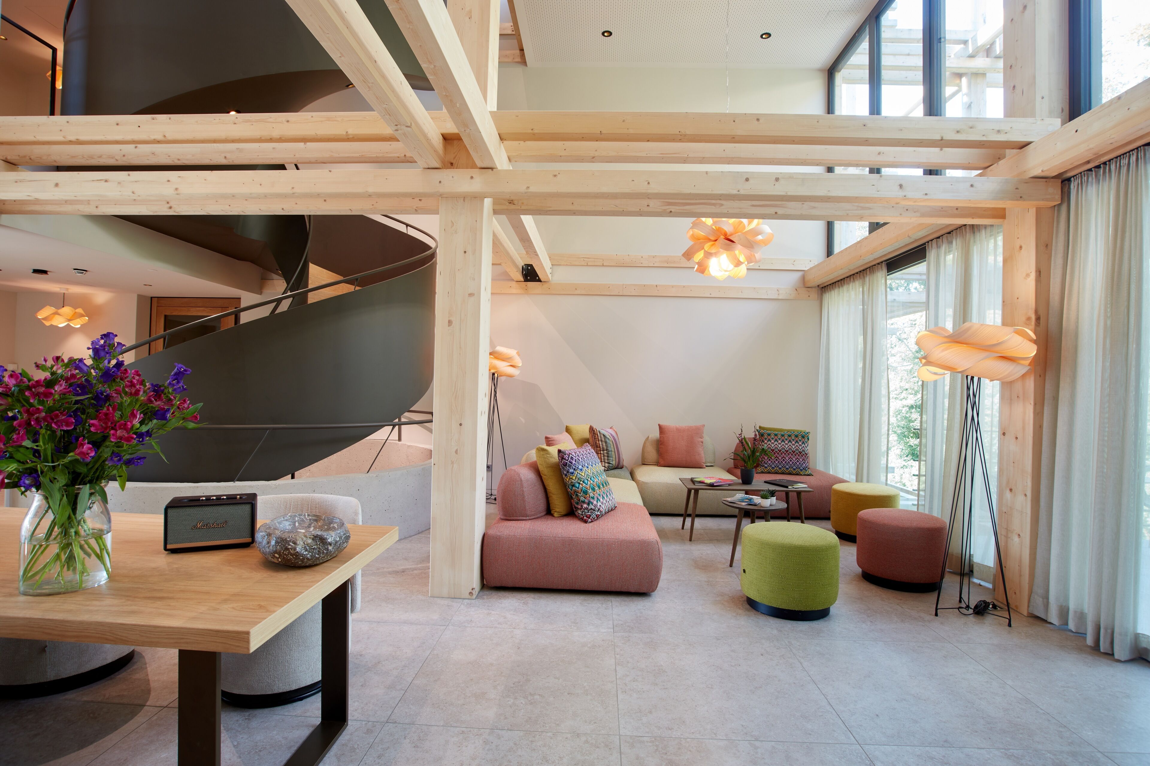 A spacious living area with a staircase, a sofa set, ottomans, and a table with a vase of flowers.