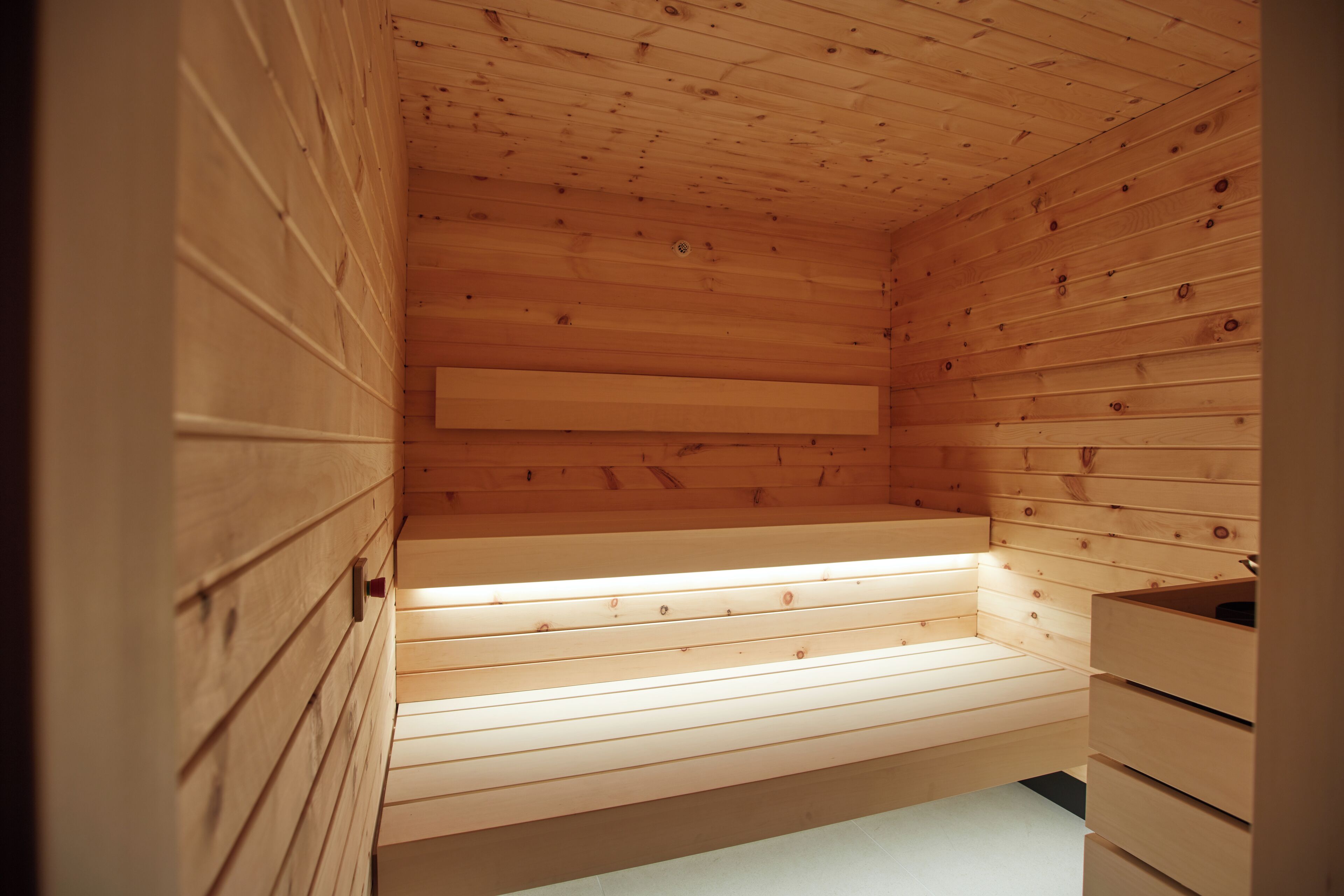 Interior de una cabaña de madera con banco, cajones y techo inclinado.