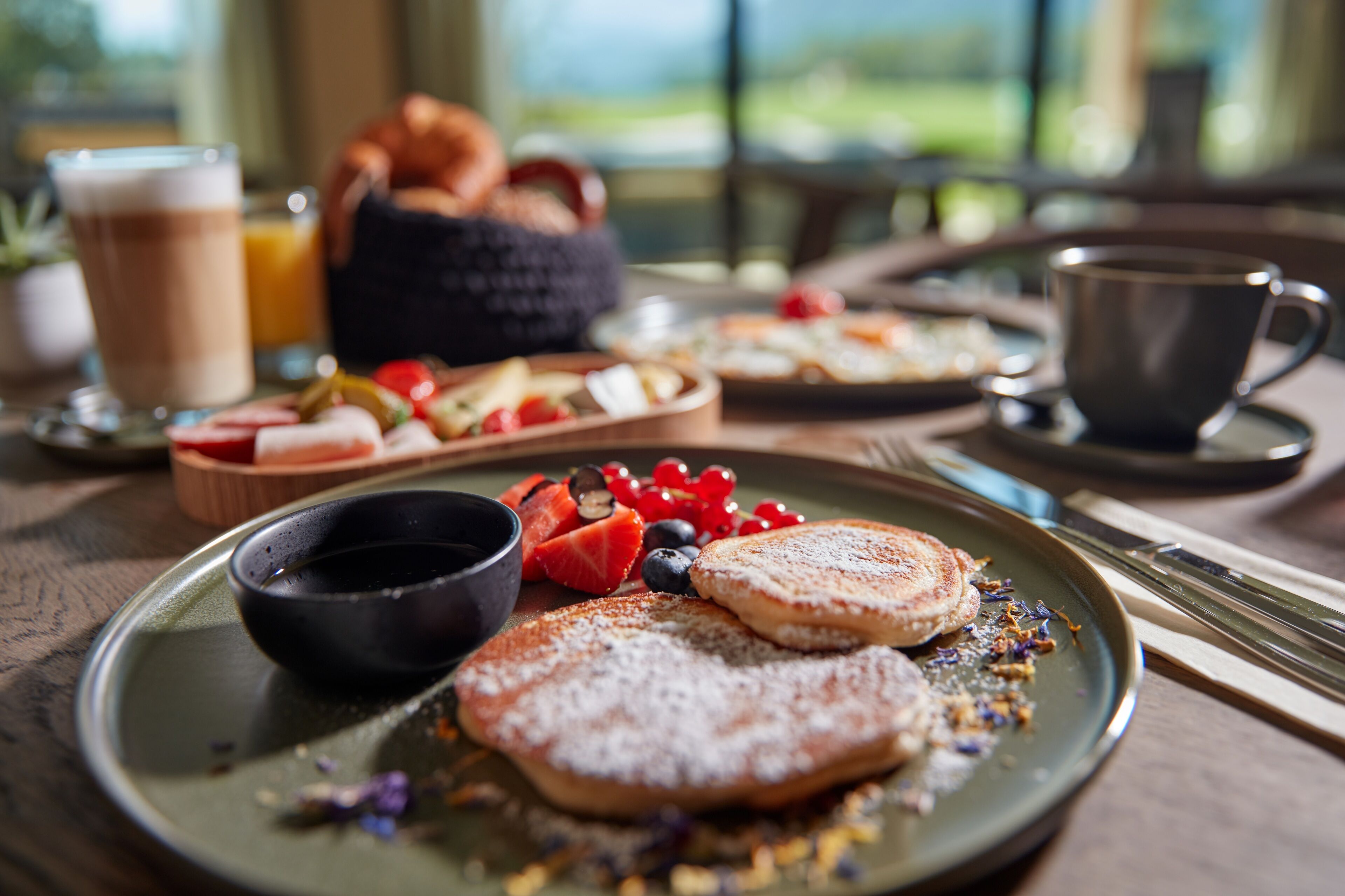 A breakfast setting with pancakes, berries, and a coffee cup on a wooden table.