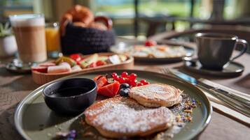 A breakfast setting with pancakes, berries, and a coffee cup on a wooden table.