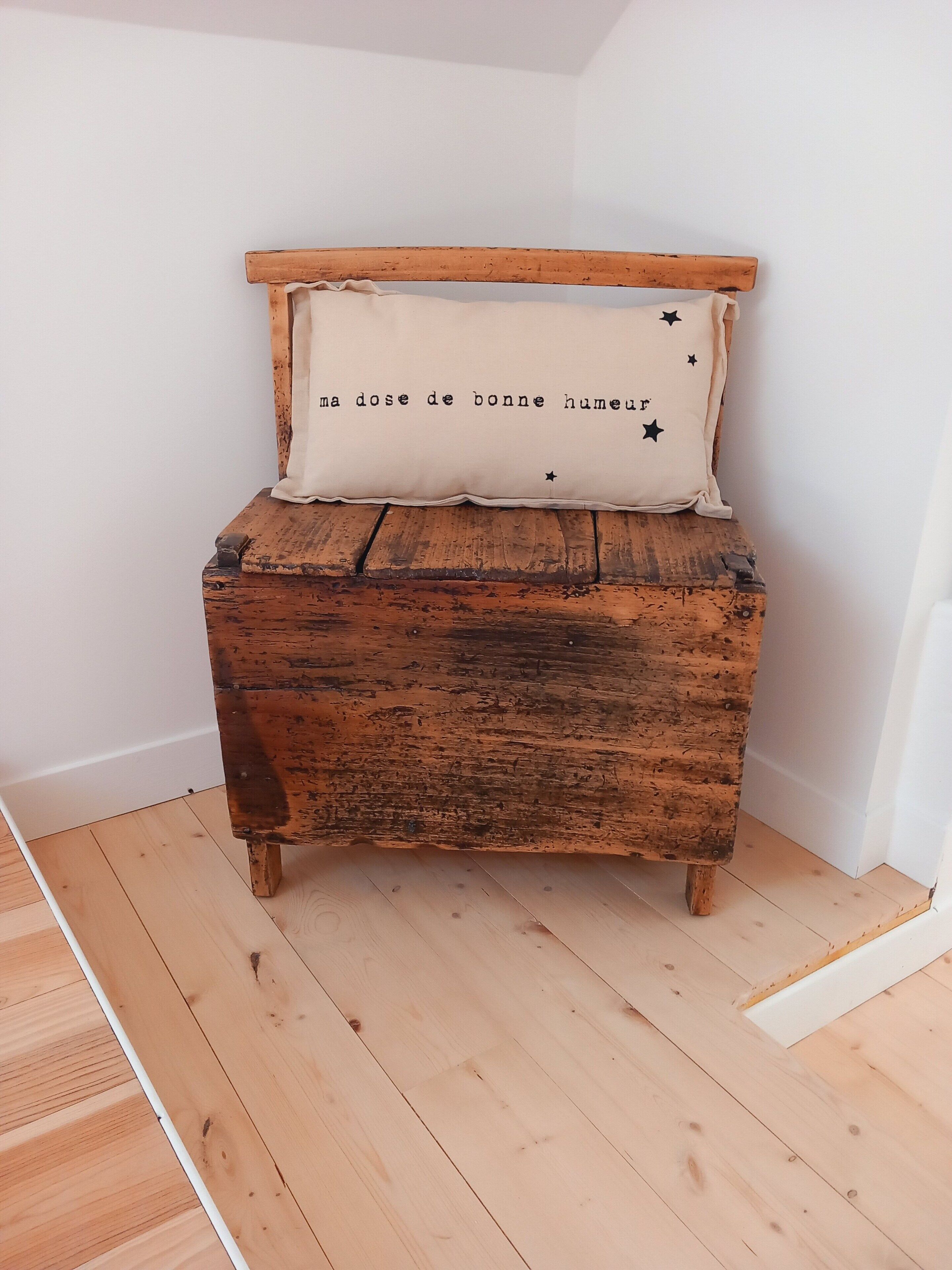 Un coffre en bois rustique, sur lequel est posé un coussin.