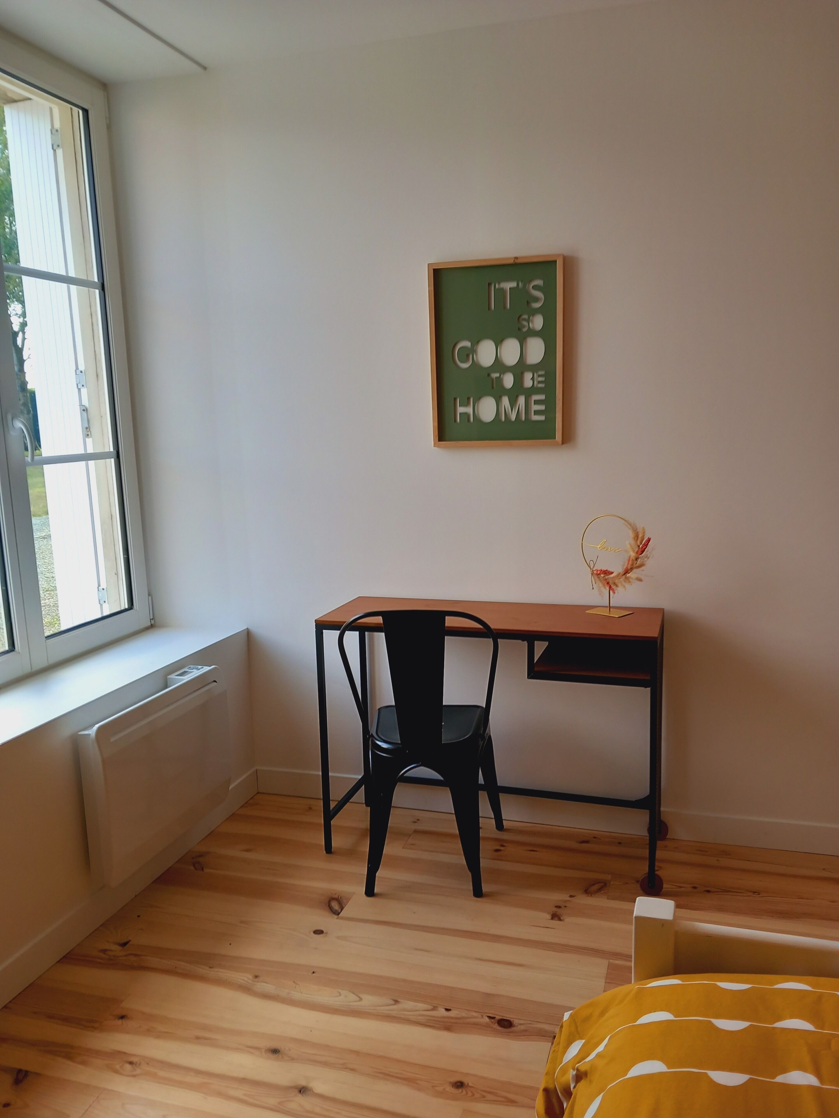 A room with a wooden desk, a black chair, a radiator, and a window.