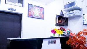 A reception desk with a 'RECEPTION' sign, a framed religious picture, and a small shrine with flowers. - Roomshala 005 Tom & Jerry (New Delhi)