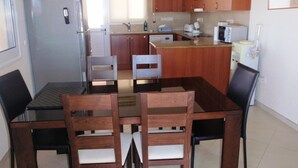 Cozinha compacta com armários de madeira, geladeira, pia e mesa de jantar com cadeiras.