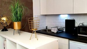 Eine moderne Küche mit weißen Schränken, einer schwarzen Arbeitsplatte, einem goldenen Drahtkorb, einem Topf mit Pflanze und einem Globus auf einem Stativ.