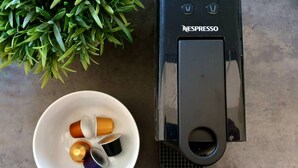Eine Nespresso-Kaffeemaschine mit weißem Tassenhalter und einer Schale mit Kapseln.