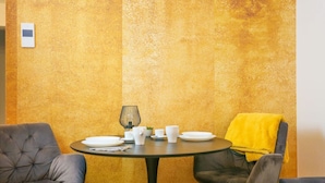 A dining area with a round table set for two, two chairs, a small lamp, and a yellow throw on one of the chairs.