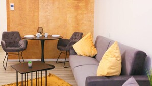 A modern living room with a gray sofa, two armchairs, a round table with a lamp, and a small potted plant.