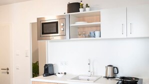 A compact kitchen with a built-in microwave, a coffee maker, a kettle, and a frying pan on the counter. - Noble Suite mit perfektem Wohn- und Arbeitskomfort (Gießen)