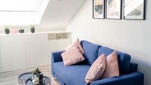 A modern living room with a blue sofa, two pink cushions, a small coffee table with a plant, and a skylight above. - Noble Suite mit perfektem Wohn- und Arbeitskomfort (Gießen)