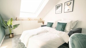 Een moderne slaapkamer met dakraam, een bed met witte lakens, een grijze fauteuil en een potplant.