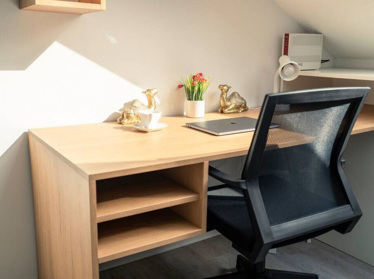 A modern workspace with a wooden desk, black mesh office chair, and decorative items including golden figurines and a potted plant.